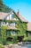 A charming inn with ivy-covered walls, large windows, and a rustic design. The building features a steep gabled roof, a central chimney, and is surrounded by a lush garden with various plants and flowers.