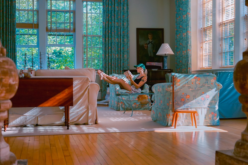 Mujer sentada en la silla del sofá floral verde azulado y rosa leyendo un libro en la habitación