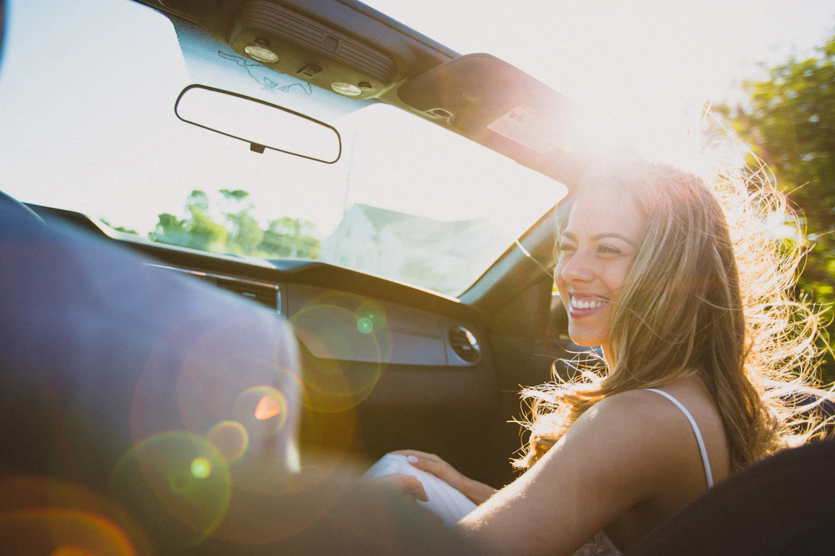 Mujer al volante mirando hacia atrás y sonriendo, con la luz del final de la tarde