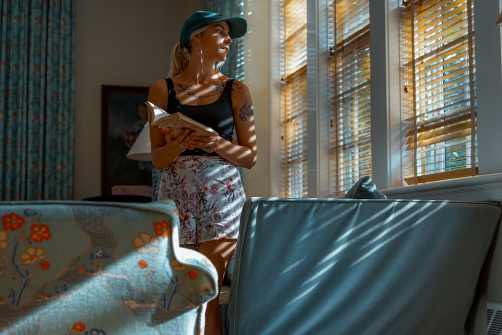 Foto Mujer sosteniendo un libro mientras de pie junto a persianas la ventana – Imagen Lectura de libros gratis en Unsplash