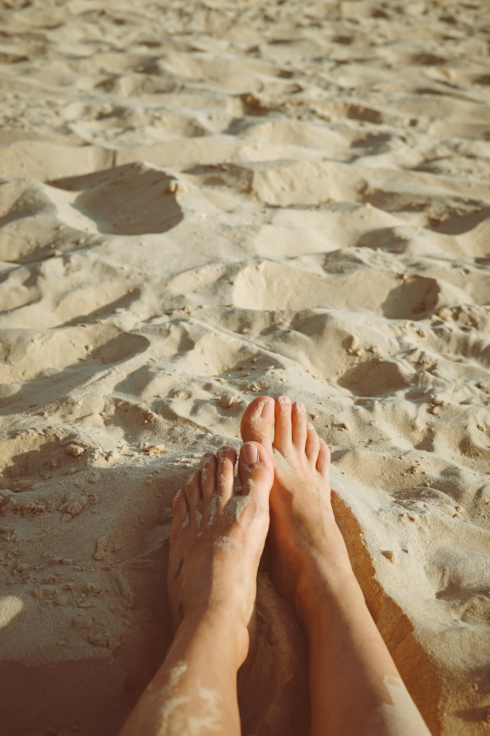 person's feet lying on sand