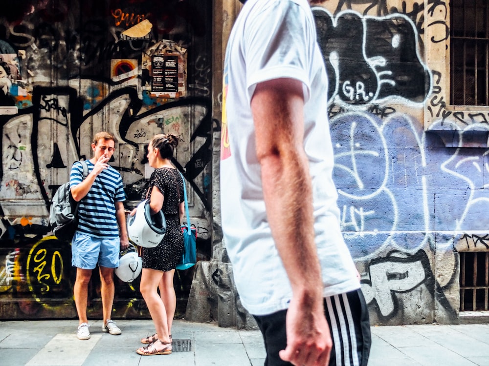 man walking on road with man and woman talking near wall in background