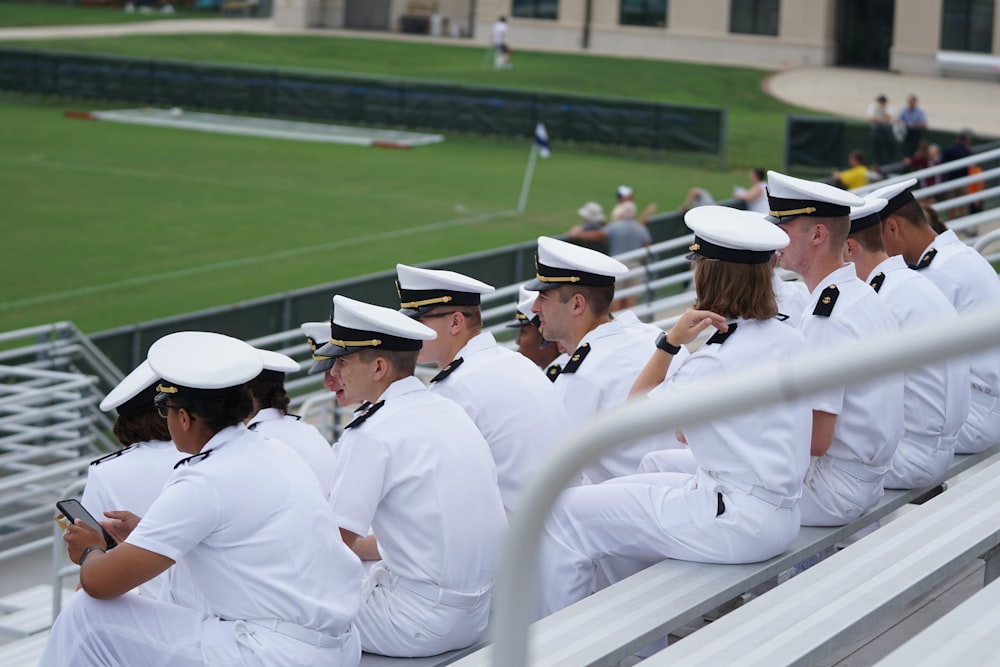 groupe de personnes en uniforme blanc assis regardant le terrain pendant la journée