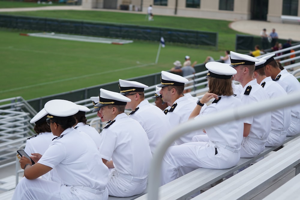 grupo de pessoas de uniforme branco sentado olhando para o campo durante o dia