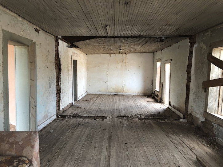 Before photo of a living room with faded, chipped walls and worn trim.
