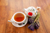 Lavender and sage herbs artfully arranged next to a rustic ceramic teapot on a wooden surface.