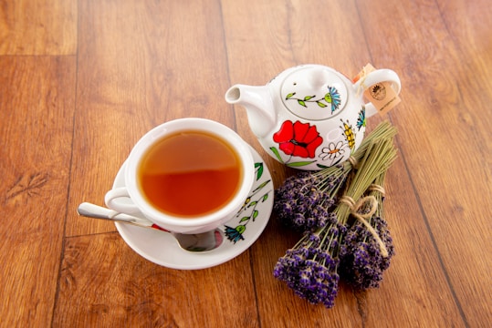 A steaming cup of tea beside scattered dried herbs and spices on a rustic wooden table.
