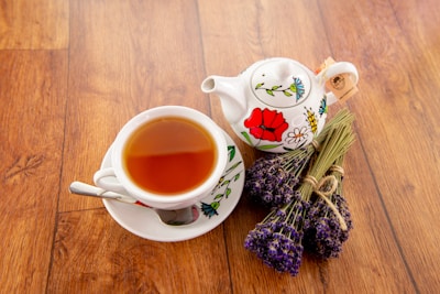 Lavender tea leaves scattered beside a dark brown ceramic tea cup.