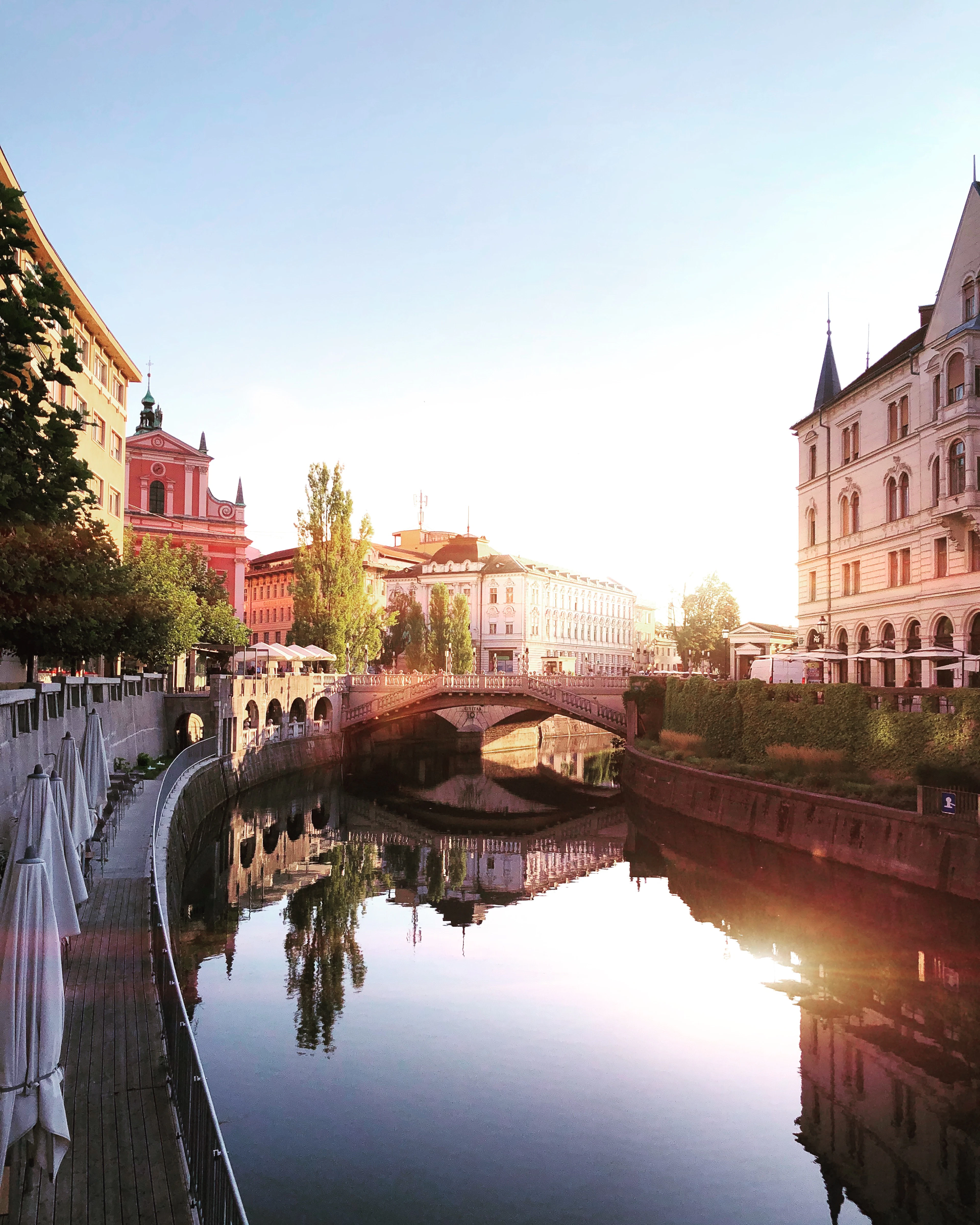 The Ljubljanica river at sunset in central Ljubljana, its calm water reflecting the bridges and the towers of the Franciscan church