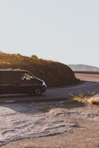 A scenic view of a Paw Voyage LLC van driving through a sunny countryside road.