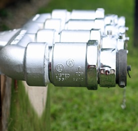 A series of shiny metallic components featuring detailed engravings and labels, indicating technical specifications. The objects appear to be connected in a line, focused in the foreground with a blurred natural background, suggesting they are outdoors.