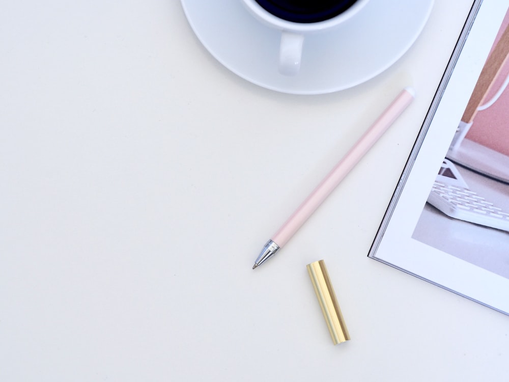 stylo rose à côté d’une tasse à thé en céramique blanche sur une surface blanche