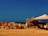A rustic outdoor market stall features a variety of terracotta pots arranged neatly on the ground. The setup includes a makeshift structure with a tarp providing shade. The background shows a vast expanse of clear sky and barren land, conveying a sense of openness and simplicity.