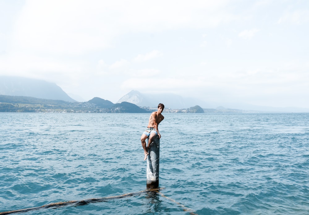 man sitting on gray post in body of water