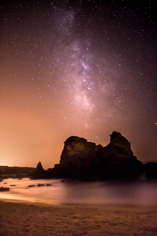 rock formation surrounded by water under black and white milky way in Porto Covo Portugal