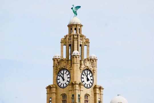 beige concrete building with two clocks under cloudy blue sky in Liverpool Waterfront United Kingdom