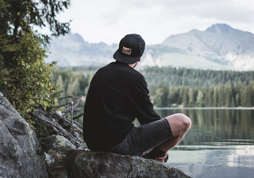 Photographie sélective de l’homme assis sur un rocher tout en regardant les montagnes