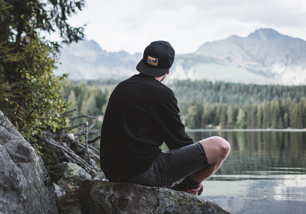 Fotografía de enfoque selectivo de hombre sentado en la roca mientras mira las montañas