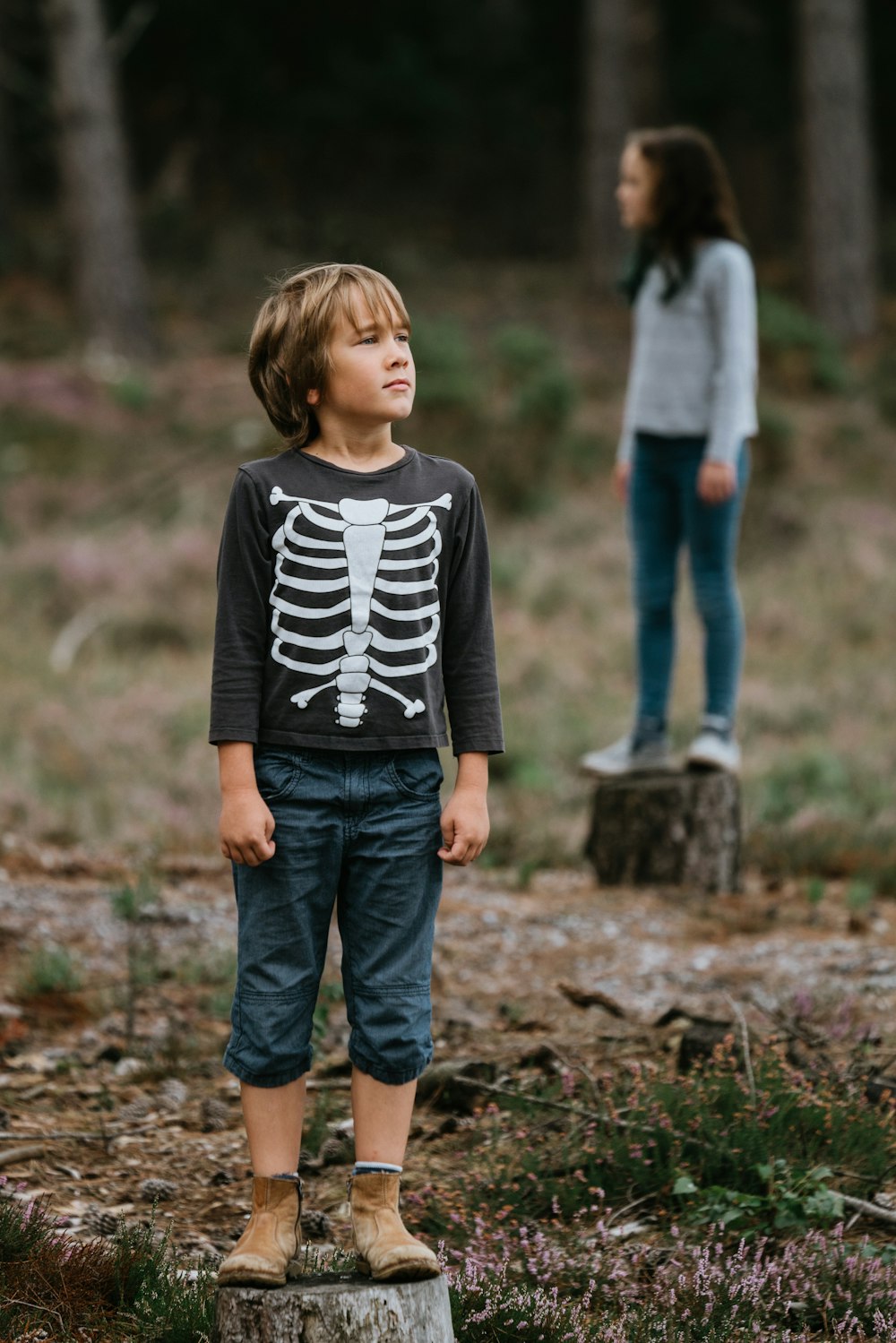 Niño con sudadera de cuello redondo estampada de esqueleto blanco y negro mientras está parado en un tronco