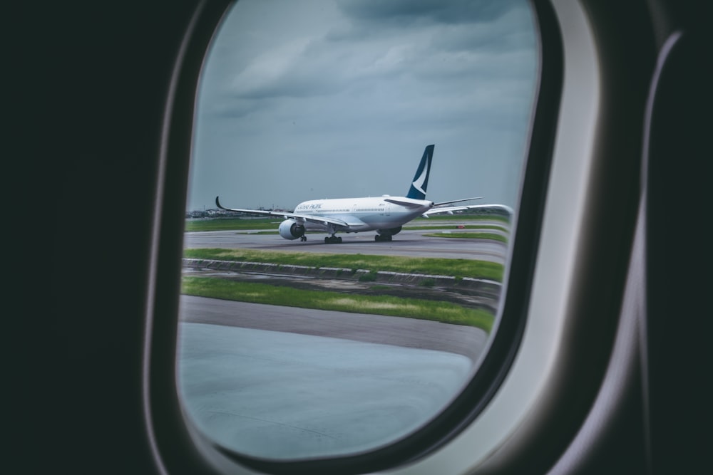 airplane window overlooking white and black airplane on gray pavement at daytime