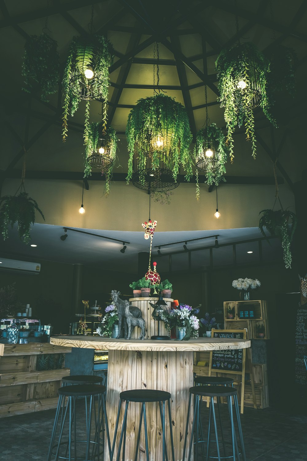 round brown wooden table surrounded by black stools under green leafed-themed pendant lamps