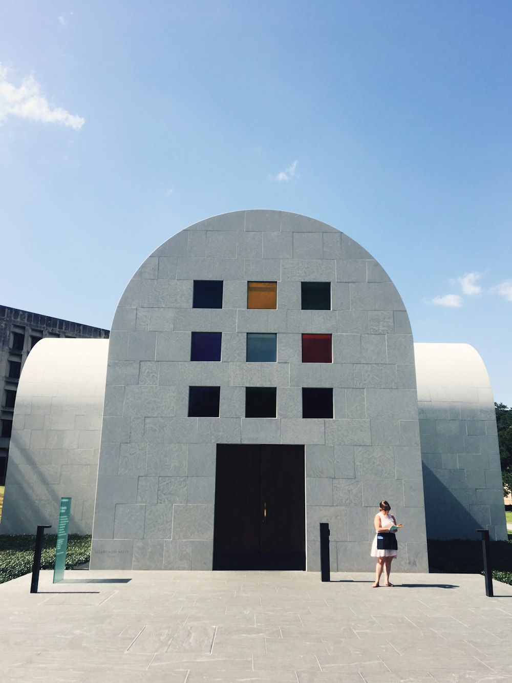 mulher que está atrás do edifício pintado de branco sob o céu azul durante o dia