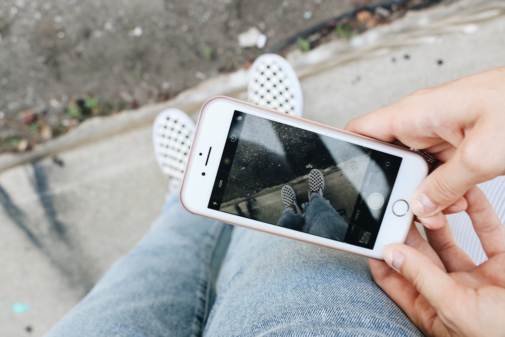 person holding rose gold iPhone 6s capturing pair of white sneakers