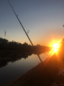 A fishing rod angled over a calm suburban lake at sunrise.