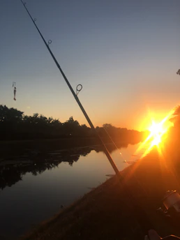 A vibrant fishing rod resting beside a calm Brazilian river at sunrise.