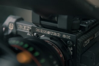 Close-up of a professional video camera with visible branding that reads MONSTRO 8K and RED. The image captures details of the camera's body, lens, and some other components with a slight focus on the text.