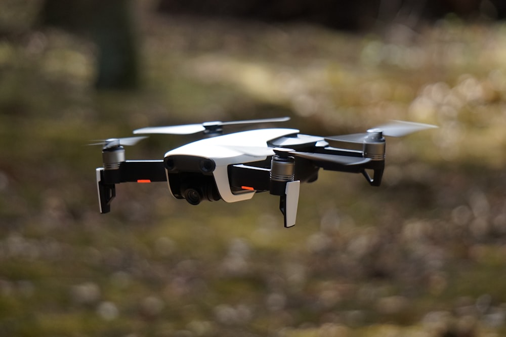 white and black quadcopter hovering on grass