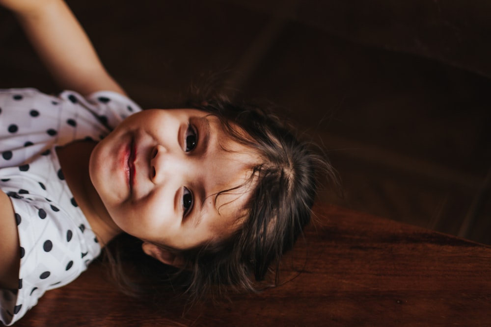 smiling girl gray and black polka-dot shirt near brown wooden wall at daytime