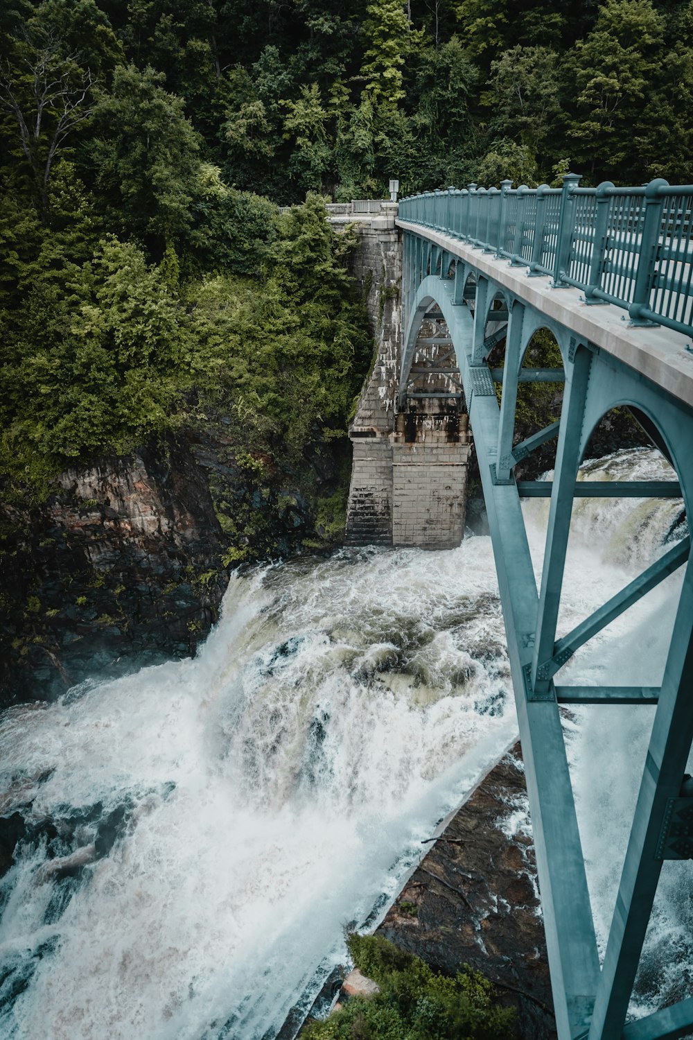 teal metal bridge across waterfalls