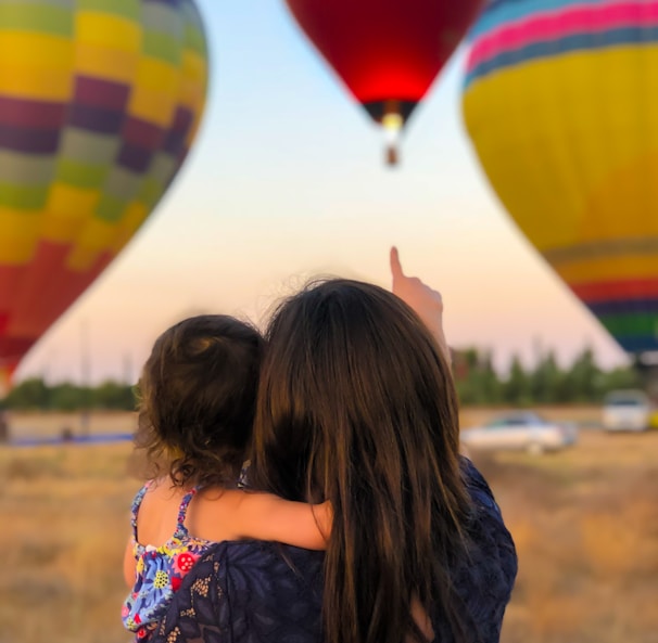 woman carrying toddler point at hot air balloon