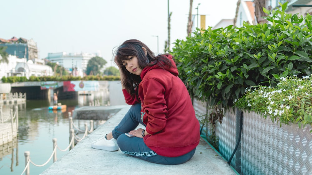 woman sitting on bank of body of water near green leafed plants at daytime