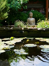 A tranquil garden with blooming lotus flowers and a small Buddha statue under soft sunlight.