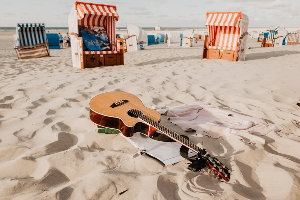 chitarra acustica marrone sulla sabbia durante il giorno