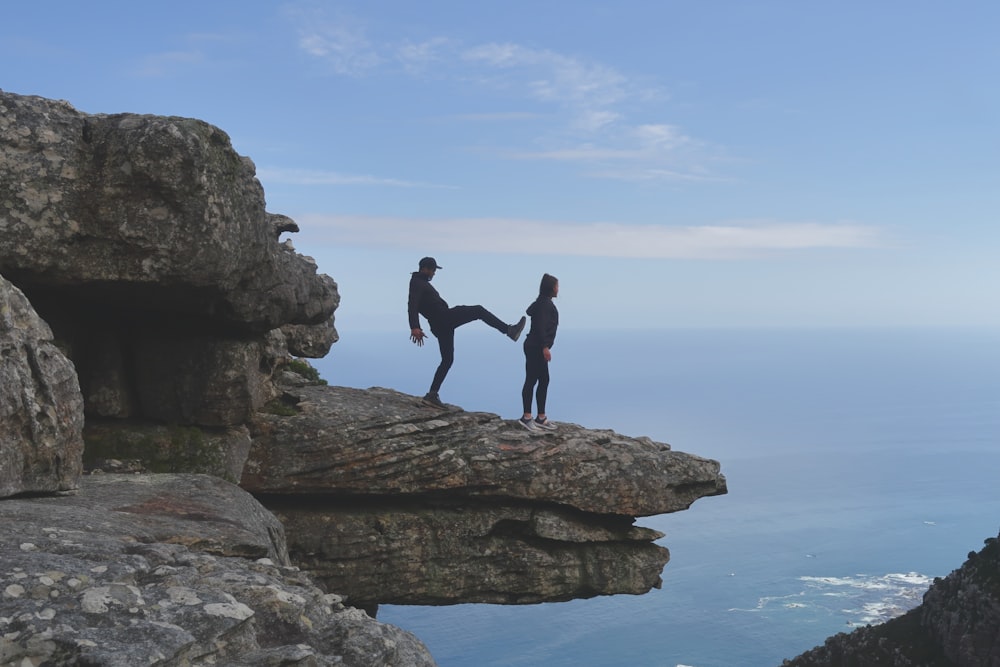 man about to kick woman standing on cliff