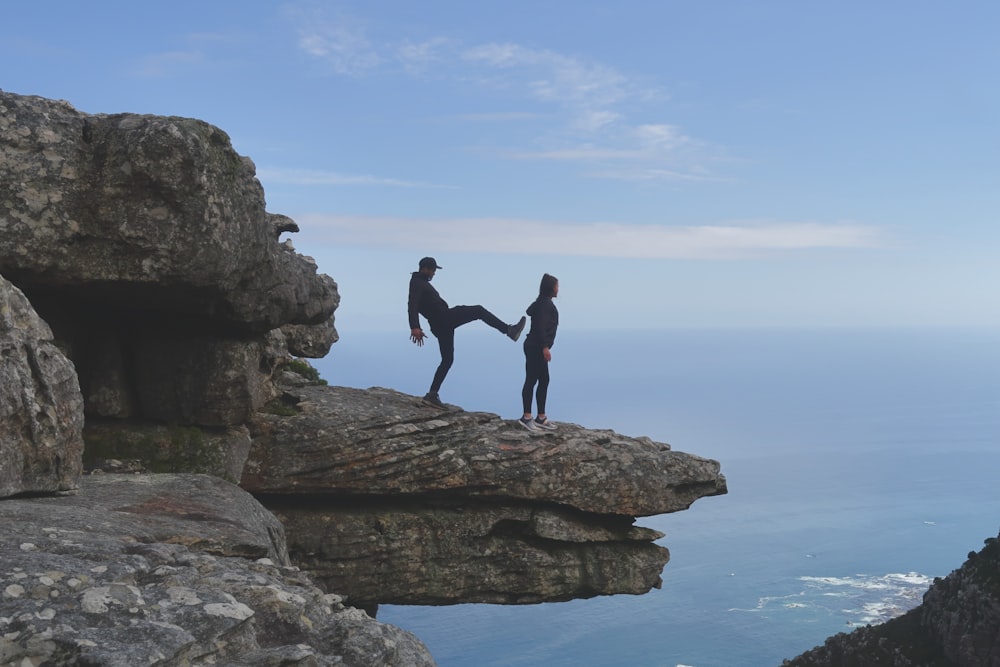 homme sur le point de donner un coup de pied femme debout sur la falaise