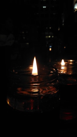 Artisan candles in glass jars with soft glowing flames on a cozy shelf.