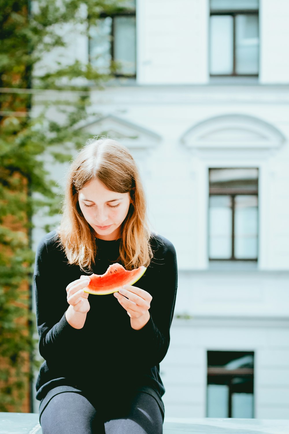 woman holding slice of watermelon while sitting on concrete bench outdoor