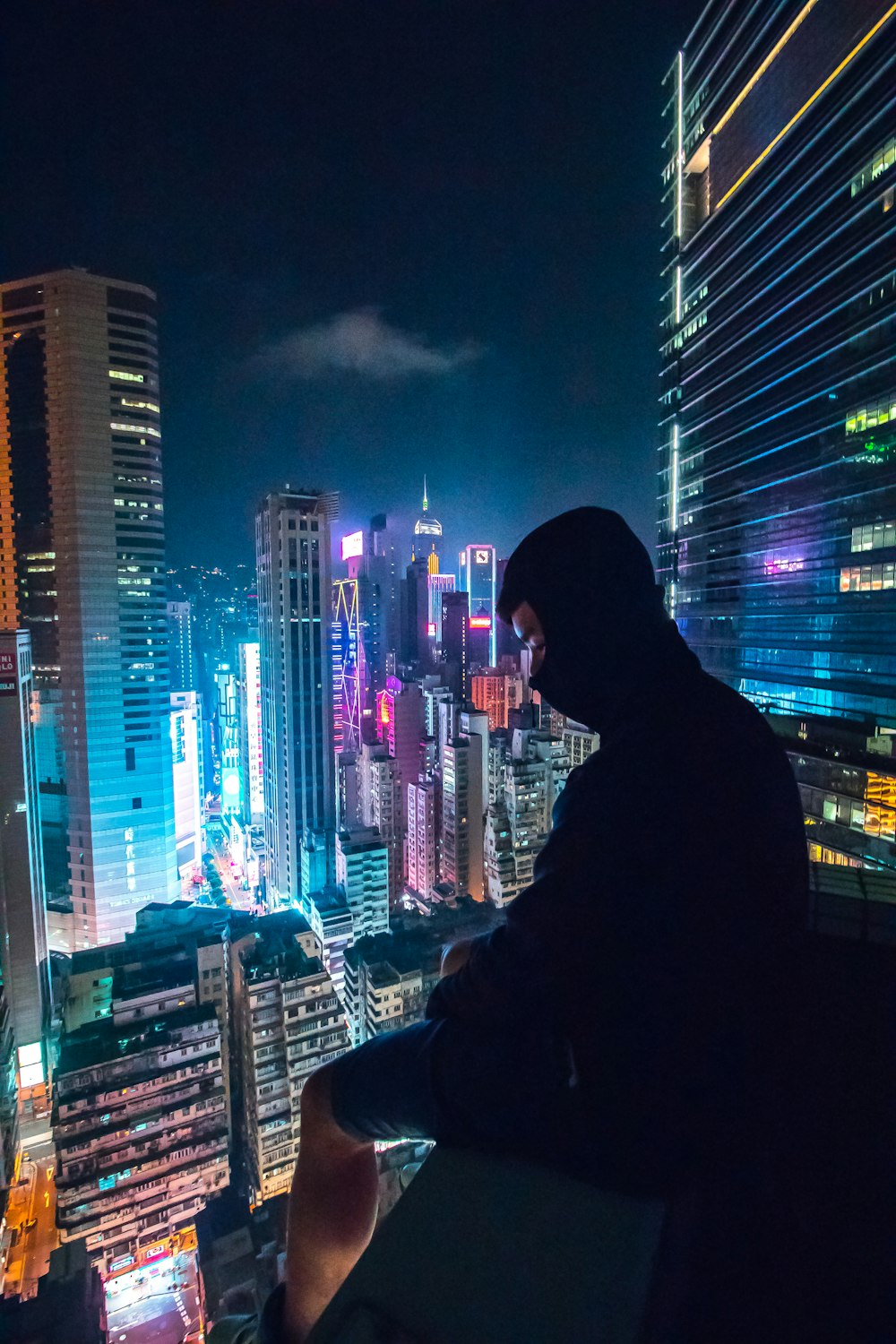 옥상에 앉아서 고층 건물이 있는 도시를 바라보고 있는 남자