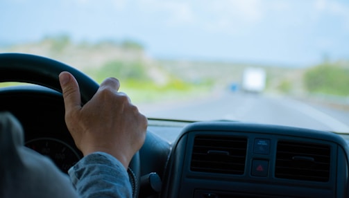 A close-up of a truck driver's hands on the steering wheel navigating an open highway.