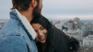 A couple smiling happily on a city rooftop with a panoramic view of a European skyline.
