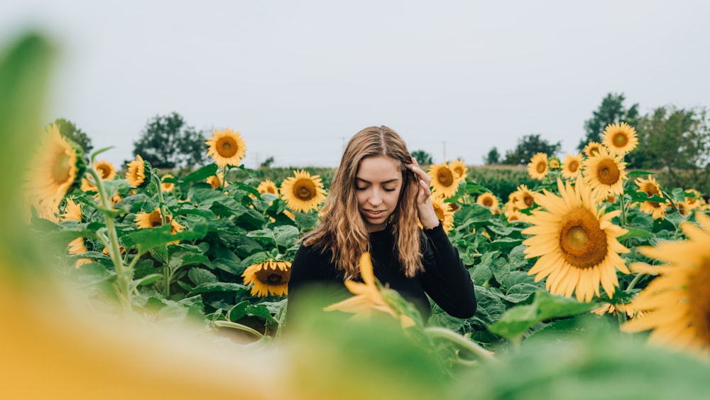 Frau in schwarzem langärmeligem Oberteil mitten im Sonnenblumenfeld während des Tages