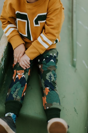 A child wearing a cozy sand-colored sweater and jeans, playing outdoors on a sunny day.