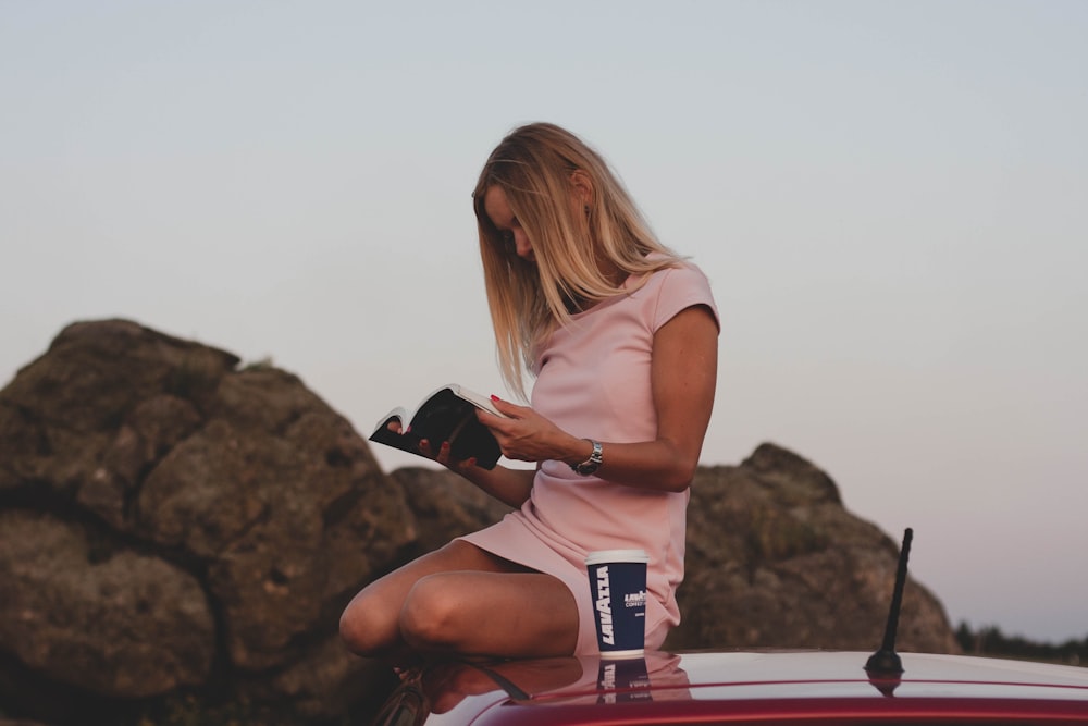 Mujer sentada en el techo del coche mientras sostiene un libro