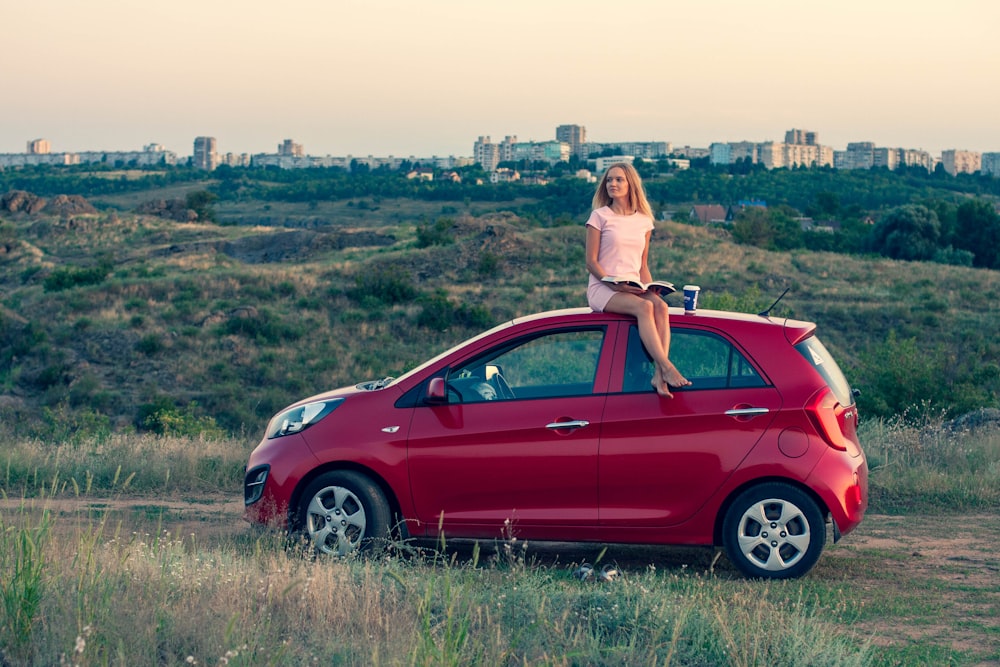 woman sitting on top of a red hatchback car