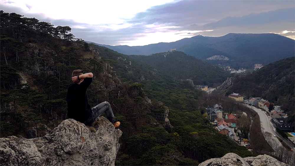 man sitting on cliff facing city