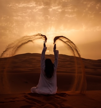 woman sitting on desert while playing sand during golden hour